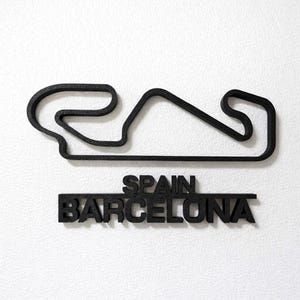 May include: A black 3D wall art piece featuring the outline of the Barcelona race track in Spain. Below the track layout, the text reads SPAIN and BARCELONA in bold, capital letters. The entire object has a textured, matte black finish.