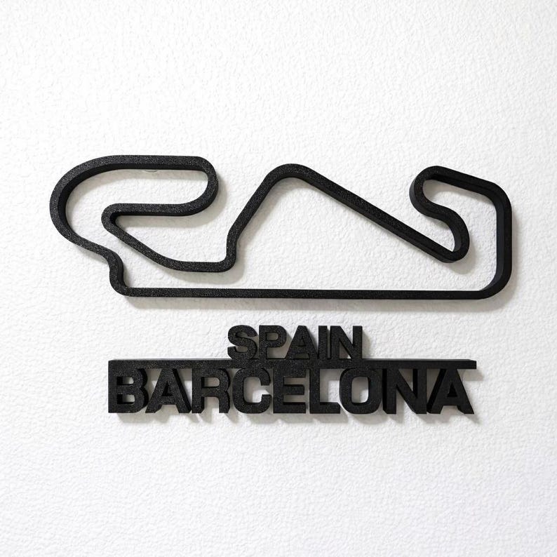 May include: A black 3D wall art piece featuring the outline of the Barcelona race track in Spain. Below the track layout, the text reads SPAIN and BARCELONA in bold, capital letters. The entire object has a textured, matte black finish.