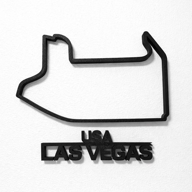 May include: A black, three-dimensional outline of the Las Vegas Grand Prix race track circuit. Below the track outline, the text "USA" is positioned above the text "LAS VEGAS" in a matching black, bold, sans-serif font style.