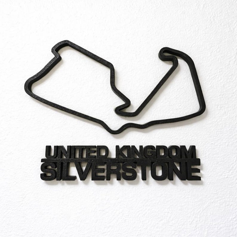 May include: A black, three-dimensional wall decoration featuring the outline of the Silverstone race track in the United Kingdom. Below the track layout, the words UNITED KINGDOM and SILVERSTONE are displayed in bold, black, capital letters.