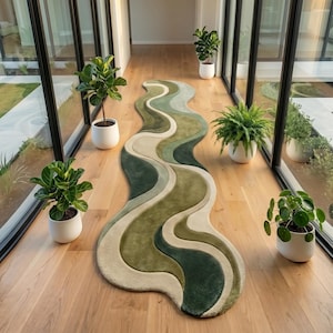 May include: A long, narrow runner rug featuring a wavy, organic shape with layered bands of color in various shades of green, olive, and cream. The rug has a soft, textured pile and is positioned on a light-colored wooden floor in a hallway.