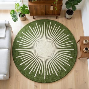 May include: A round green rug with a white sunburst design. The rug has a soft, textured appearance and is placed on a light-colored wooden floor. The rug's design features a central off-white circle with radiating white lines.