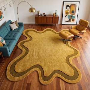 May include: A large, irregularly shaped area rug featuring a central mustard yellow section surrounded by a wavy, dark olive green border. The rug has a soft, plush texture and follows a fluid, organic outline that covers a significant portion of the floor.