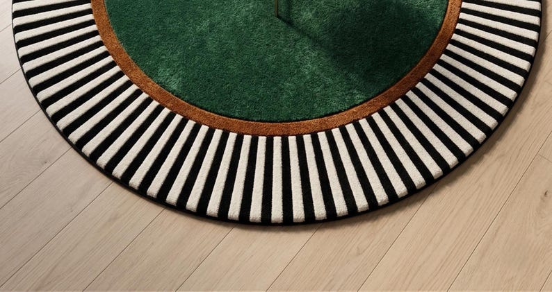 May include: A round rug with a green center, a brown border, and a black and white striped outer edge. The rug is on a light wood floor. The design is modern and geometric.