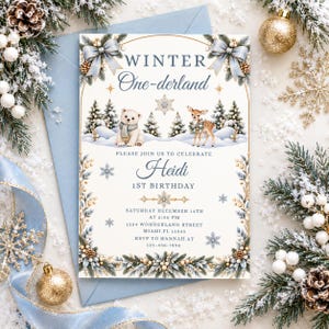 Puede incluir: Una tarjeta de invitación rectangular con el texto Winter One-derland, Heidi 1st Birthday y detalles del evento. El diseño incluye ilustraciones de un oso polar, un cervatillo, pinos, copos de nieve y lazos azules sobre un fondo blanco.