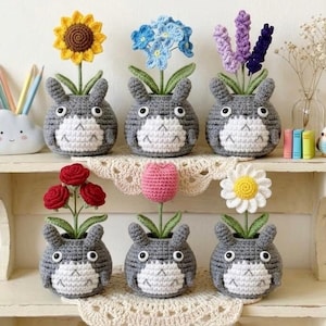 May include: Six crocheted gray creatures with white bellies and ears, each holding a different flower: a yellow sunflower, blue forget-me-nots, purple lavender, three red roses, a pink tulip, and a white daisy with a yellow center.