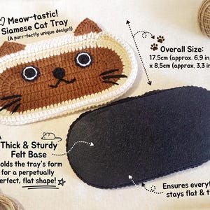 May include: An oval Siamese cat tray with brown and cream crochet detailing, featuring embroidered eyes, nose, and whiskers. The tray includes a thick, sturdy black felt base. The overall dimensions are 17.5 cm wide by 8.5 cm high, or 6.9 inches by 3.3 inches.