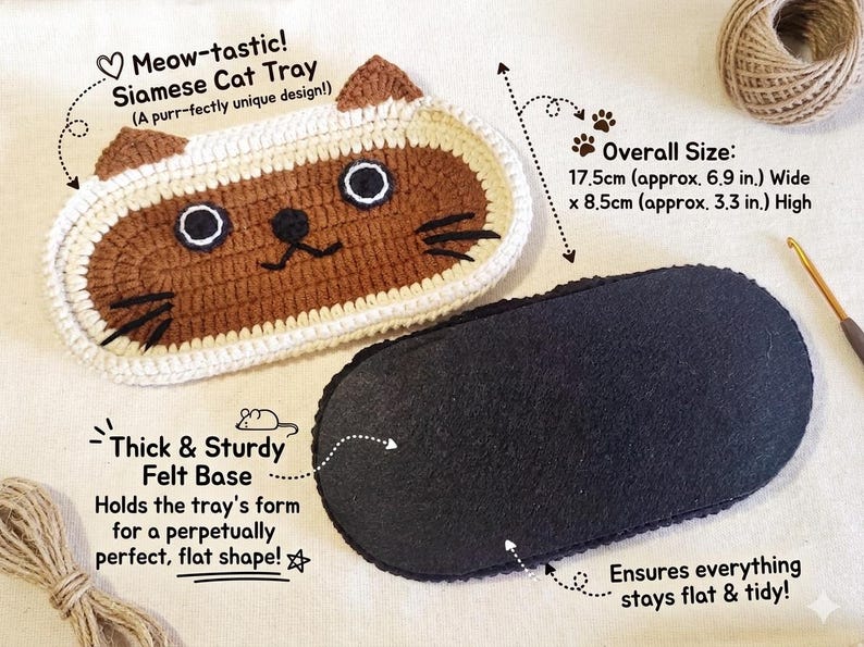 May include: An oval Siamese cat tray with brown and cream crochet detailing, featuring embroidered eyes, nose, and whiskers. The tray includes a thick, sturdy black felt base. The overall dimensions are 17.5 cm wide by 8.5 cm high, or 6.9 inches by 3.3 inches.