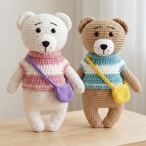 Könnte beinhalten: Zwei gehäkelte Teddybären stehen nebeneinander. Der linke Bär ist weiß mit einem rosa-weiß gestreiften Pullover und einer lila Umhängetasche. Der rechte Bär ist hellbraun mit weißer Schnauze, blau-weiß gestreiftem Pullover und gelber Tasche.