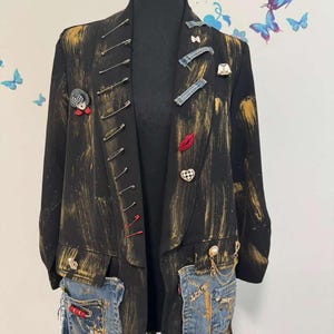 May include: Black blazer with gold paint strokes and denim pocket accents. The blazer is adorned with safety pins, decorative pins, and a red embroidered lip. The pockets have the word "LOVE" on them.