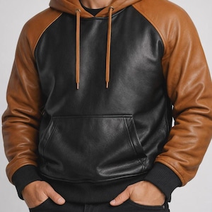 Puede incluir: Una sudadera con capucha de manga larga que presenta un panel frontal y trasero negro con mangas y capucha de color tostado. La prenda incluye un bolsillo tipo canguro, una capucha con cordones tostados y puños y dobladillo acanalados en negro.