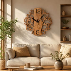 Può includere: Un orologio da parete circolare realizzato in legno marrone chiaro, caratterizzato da un design centrale a tronco d'albero con rami che si estendono verso l'esterno. Il quadrante mostra grandi numeri ritagliati da uno a dodici, con lancette nere.