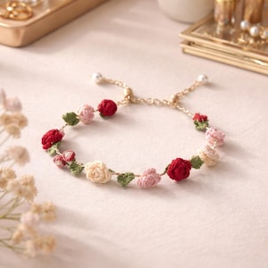 Può includere: Un braccialetto delicato con rose all'uncinetto rosse, rosa e crema, con foglie verdi. La catena dorata ha una perla a ciascuna estremità. Un gioiello floreale per un look femminile e romantico.