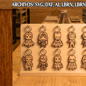 Puede incluir: Un expositor de madera clara con diez llaveros de madera cortados a láser que representan superhéroes de estilo chibi. El texto ARCHIVOS: SVG, DXF, AI, LBRN, LBRN2, PDF es visible en la parte superior y el logo URBAN TITANS está abajo a la izquierda.