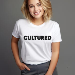 May include: A white short-sleeved t-shirt featuring the word CULTURED printed in bold black capital letters across the chest. The garment has a classic crew neckline and a standard fit, providing a clean and simple aesthetic for casual wear.