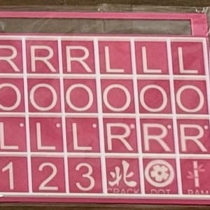May include: A pink Scrabble tile set with white letter tiles. The tiles spell out "ROLL" and "LILL" with additional letters and numbers. The set includes special character tiles with Japanese symbols and the words "CRACK DOT RAM".