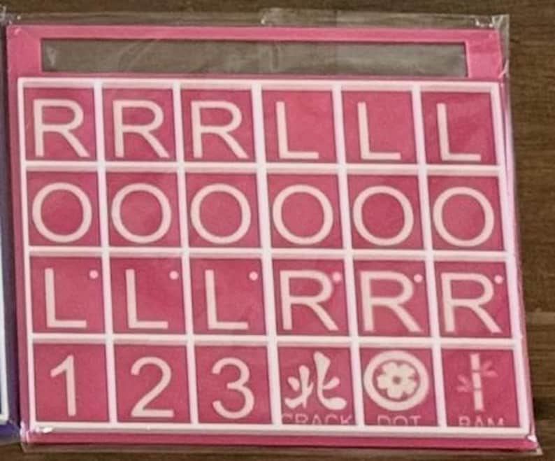 May include: A pink Scrabble tile set with white letter tiles. The tiles spell out "ROLL" and "LILL" with additional letters and numbers. The set includes special character tiles with Japanese symbols and the words "CRACK DOT RAM".