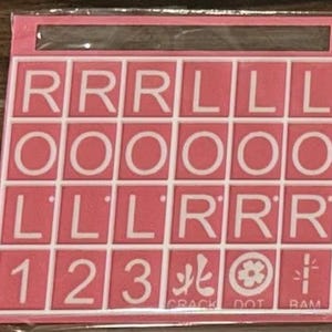 May include: Pink and white Scrabble tile set with letters, numbers, and symbols. The tiles are arranged in a grid, with the letters R, O, and L appearing multiple times. The set includes the numbers 1, 2, and 3, along with symbols and the words CRACK, DOT, and RAM.