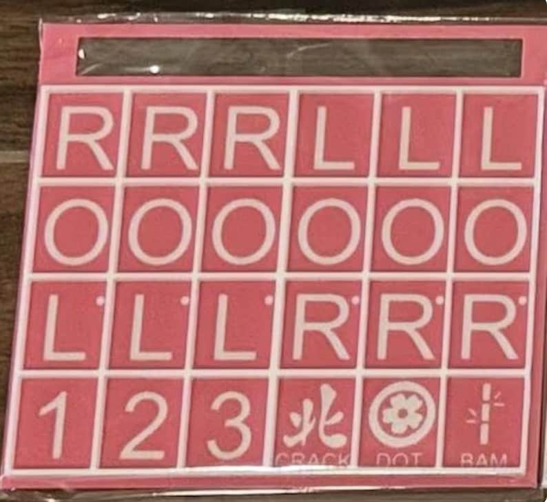 May include: Pink and white Scrabble tile set with letters, numbers, and symbols. The tiles are arranged in a grid, with the letters R, O, and L appearing multiple times. The set includes the numbers 1, 2, and 3, along with symbols and the words CRACK, DOT, and RAM.
