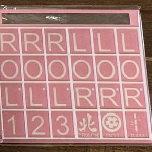 May include: A pink Scrabble tile set with white letters and numbers. The tiles include the letters R, L, and O, along with the numbers 1, 2, and 3. The set also includes symbols and the text "CRACK DOT RAM".