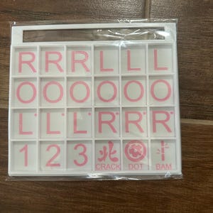May include: A white plastic tile set with pink letters and numbers. The set includes the letters R, L, and O, along with the numbers 1, 2, and 3. The text "CRACK DOT BAM" is also included.