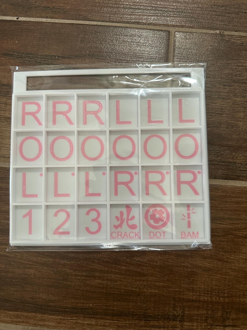 May include: A white plastic tile set with pink letters and numbers. The set includes the letters R, L, and O, along with the numbers 1, 2, and 3. The text "CRACK DOT BAM" is also included.