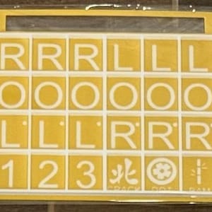 May include: A yellow and white tile set with letters and numbers. The tiles are arranged in a grid pattern, with letters like "R" and "L" and numbers "1", "2", and "3". The set also includes Japanese characters and symbols.