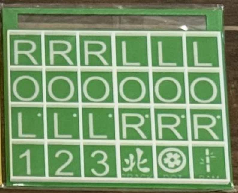 May include: A green and white game board with a grid of letter and number tiles. The tiles display the letters R, O, and L, along with the numbers 1, 2, and 3. The game board also includes symbols and characters.