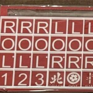 May include: A red and white tile set with letters, numbers, and symbols. The tiles are arranged in a grid, with the letters "R", "O", and "L" prominently displayed. Numbers 1, 2, and 3 are also present, along with Chinese characters and symbols.