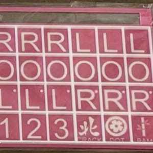 May include: Pink and white tile set with letters, numbers, and symbols. The tiles are arranged in a grid, with the letters spelling out "RRRLLLOOOOLLLLRRR" and numbers 1, 2, and 3. The bottom row has symbols and the words "CRACK DOT DAM".