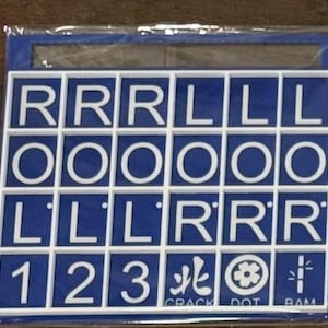 May include: A blue and white letter and number tile set. The tiles are arranged in a grid, with letters and numbers. The bottom row includes the numbers 1, 2, and 3, along with three symbols and the words "CRACK", "DOT", and "RAM".
