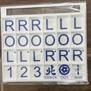 May include: A white game tile set with blue lettering and symbols. The set includes letter tiles with the letters R, L, and O, along with number tiles 1, 2, and 3. The set also includes tiles with the words CRACK, DOT, and BAM.