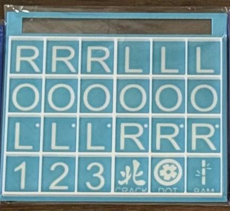 May include: A Scrabble tile set with white letter tiles on a light blue background. The tiles spell out the word "ROLL" multiple times, along with numbers and symbols. The set is contained within a light blue frame.