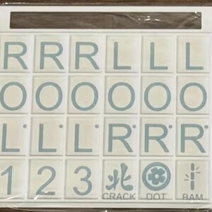 May include: A white tile game board with light blue letters and numbers. The tiles spell out letters and numbers, with the words "CRACK", "DOT", and "BAM" at the bottom. The game board is in a white frame.