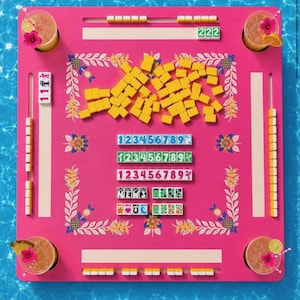 May include: A vibrant pink Mahjong game set with yellow tiles and floral accents. The set includes number tiles, dice, and four cocktails with flower garnishes. The game is set against a blue water background.