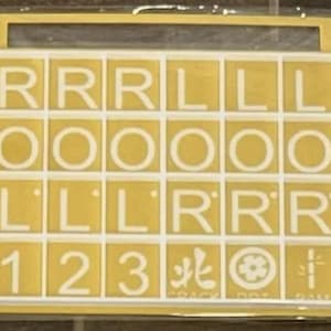 May include: A yellow stencil with white letters and numbers. The letters include R, L, and O. Numbers 1, 2, and 3 are also present. Symbols and the text "CRACK DOT FAN" are included. The stencil is in a clear plastic case.