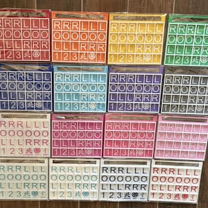 May include: A collection of colorful Scrabble tile sets in various colors, including red, orange, yellow, green, blue, purple, white, pink, and black. Each set contains letter tiles and number tiles, perfect for word games.