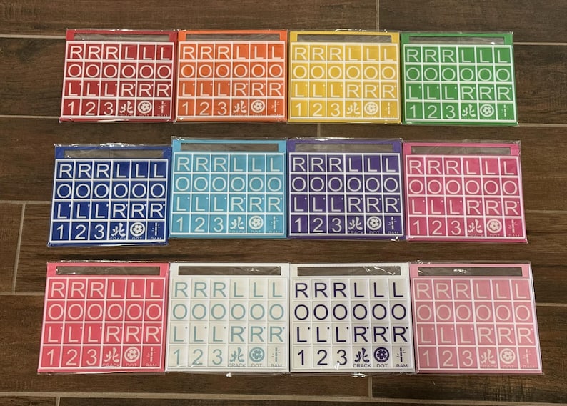 May include: A collection of colorful Scrabble tile sets, each in a different color, including red, orange, yellow, green, blue, teal, purple, pink, white, and light pink. Each set contains letter tiles and number tiles.