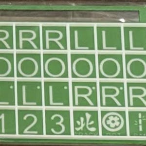 May include: A green and white game board with a grid of squares containing letters, numbers, and symbols. The letters include R, L, and O. Numbers 1, 2, and 3 are also present. The board is in a green frame.
