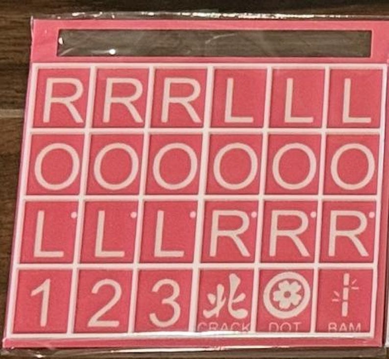 May include: A pink game board with white letter and number tiles. The tiles spell out letters and numbers, including the numbers 1, 2, and 3. The bottom row includes the words "CRACK", "DOT", and "RAM".