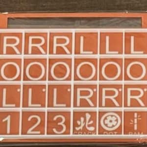 May include: An orange and white tile game with letters, numbers, and symbols. The tiles are arranged in a grid, with letters like R, L, and O, numbers 1, 2, and 3, and various symbols. The game is in a box.
