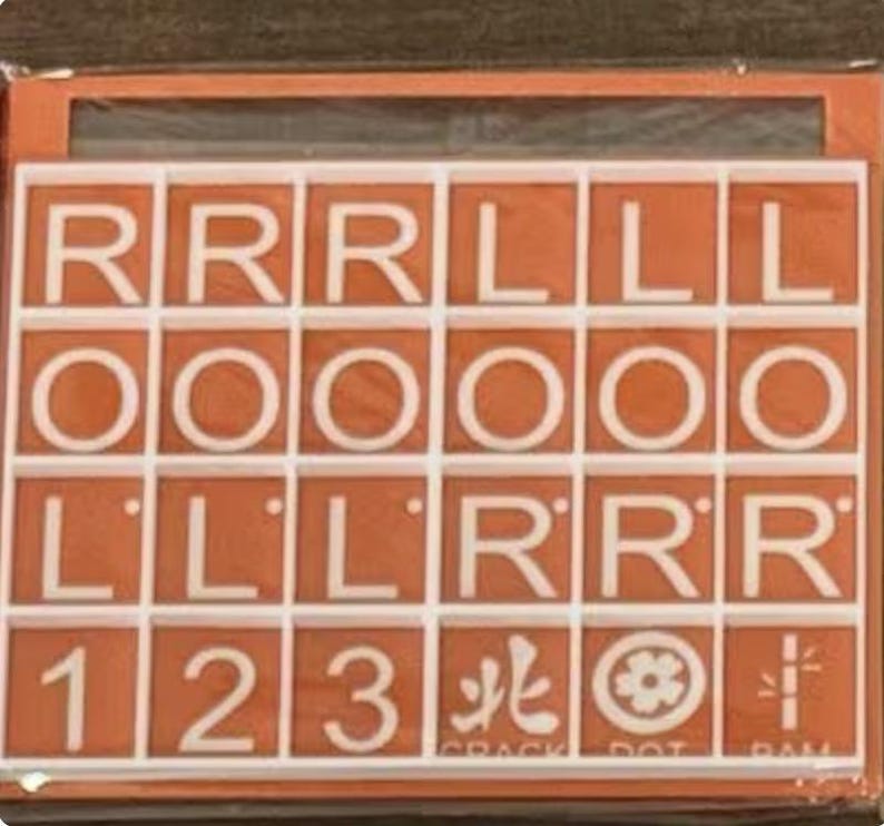 May include: An orange and white tile game with letters, numbers, and symbols. The tiles are arranged in a grid, with letters like R, L, and O, numbers 1, 2, and 3, and various symbols. The game is in a box.
