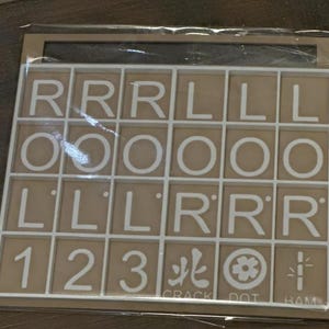 May include: A beige-colored game board with a white grid containing letter tiles and number tiles. The letters include R, L, and O. Numbers 1, 2, and 3 are also present, along with symbols and the words "CRACK", "DOT", and "RAM".