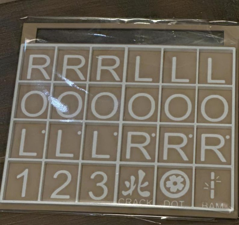 May include: A beige-colored game board with a white grid containing letter tiles and number tiles. The letters include R, L, and O. Numbers 1, 2, and 3 are also present, along with symbols and the words "CRACK", "DOT", and "RAM".