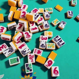 May include: A collection of Mahjong tiles scattered on a teal surface. The tiles are white with red numbers and symbols, and some have yellow or purple accents. Several tiles are marked with the word "Joker".