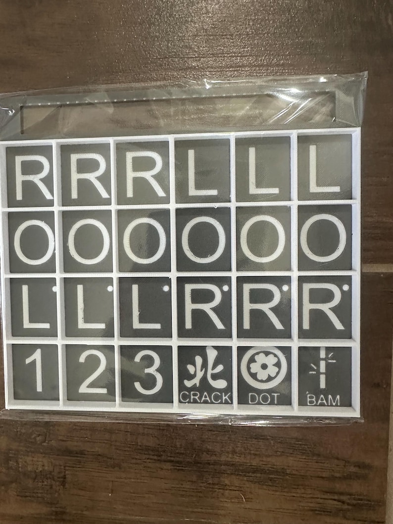 May include: A set of gray tiles with white letters, numbers, and symbols. The tiles spell out the letters R, L, and O, the numbers 1, 2, and 3, and the words CRACK, DOT, and BAM. The tiles are in a white plastic frame.