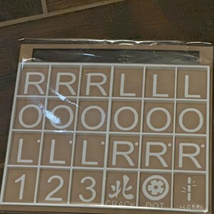 May include: A tan-colored game board with white grid lines and letter tiles. The tiles display the letters R, L, and O, along with the numbers 1, 2, and 3. The board also includes the words "CRACK", "DOT", and "RAM".
