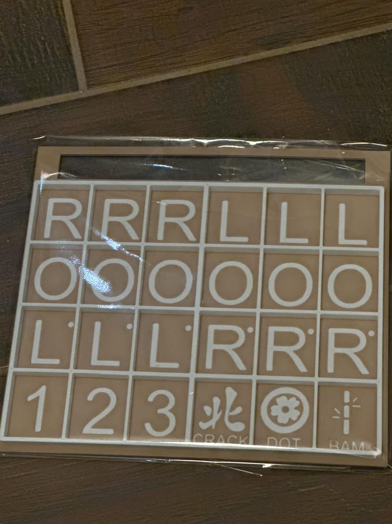 May include: A tan-colored game board with white grid lines and letter tiles. The tiles display the letters R, L, and O, along with the numbers 1, 2, and 3. The board also includes the words "CRACK", "DOT", and "RAM".