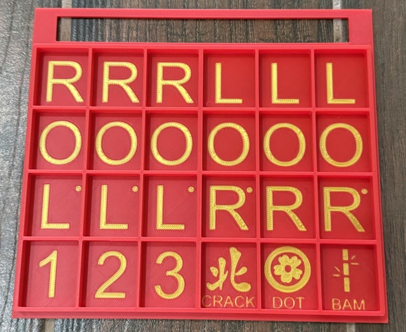 May include: A red game board with a handle, featuring gold letters, numbers, and symbols. The board is divided into squares, displaying letters like "R" and "L", numbers "1", "2", and "3", and symbols with the words "CRACK", "DOT", and "BAM".