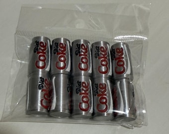 May include: A set of ten miniature silver-colored soda cans arranged in two rows of five inside a clear plastic bag. Each small cylindrical item features the red and black Diet Coke logo printed on the front with a white curved graphic accent.